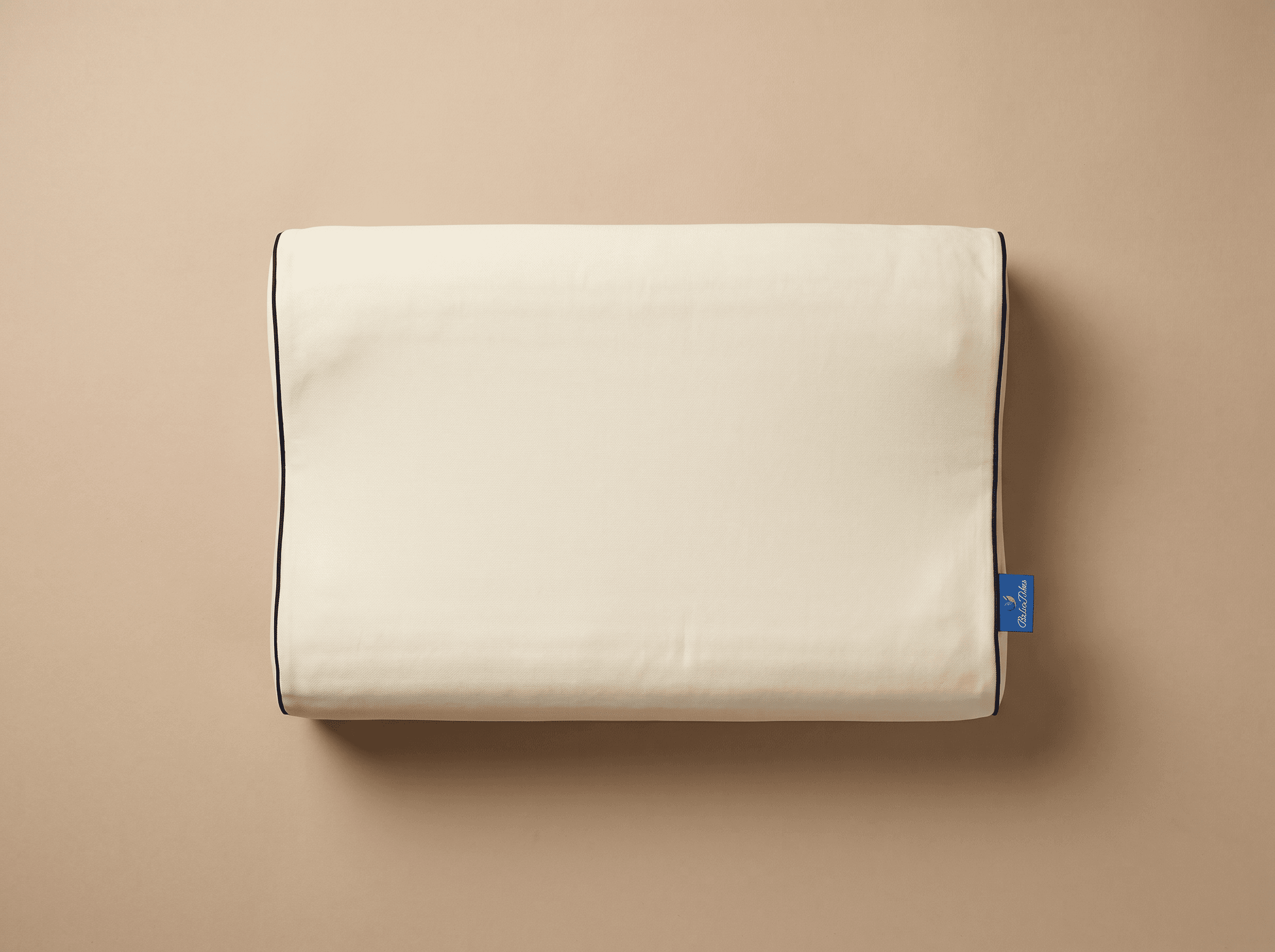 Top-down editorial photo of the Belor Pulse pillow showcasing the smooth beige texture and piping finish